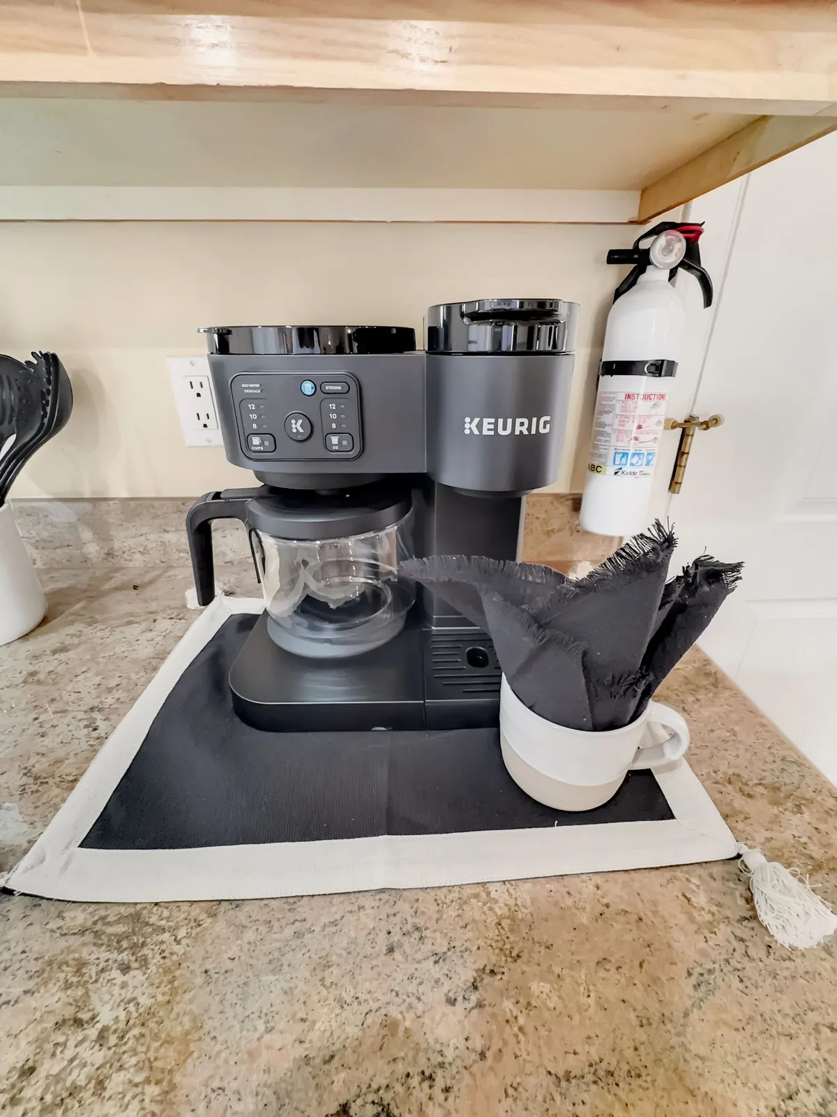 A cozy, inviting countertop scene featuring a Keurig coffee maker, black napkins, a white mug, and distinctive countertop texture, evoking the aroma and ritual of morning coffee.