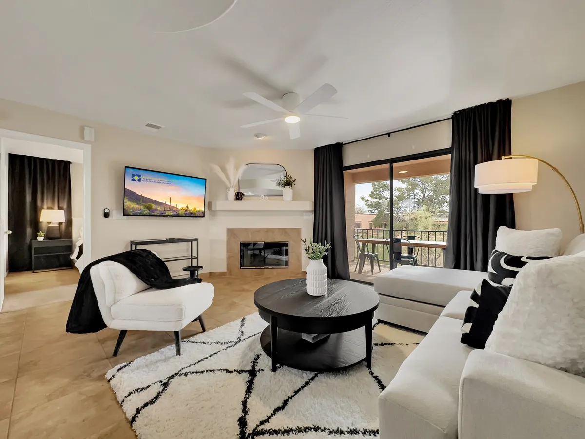 A spacious, modern living room featuring a plush sofa, stylish coffee table, television, fireplace, and a large window that fills the space with natural light and offers views outside. The room is thoughtfully arranged for both relaxation and socializing, setting a welcoming, hotel-like tone as you enter the home.