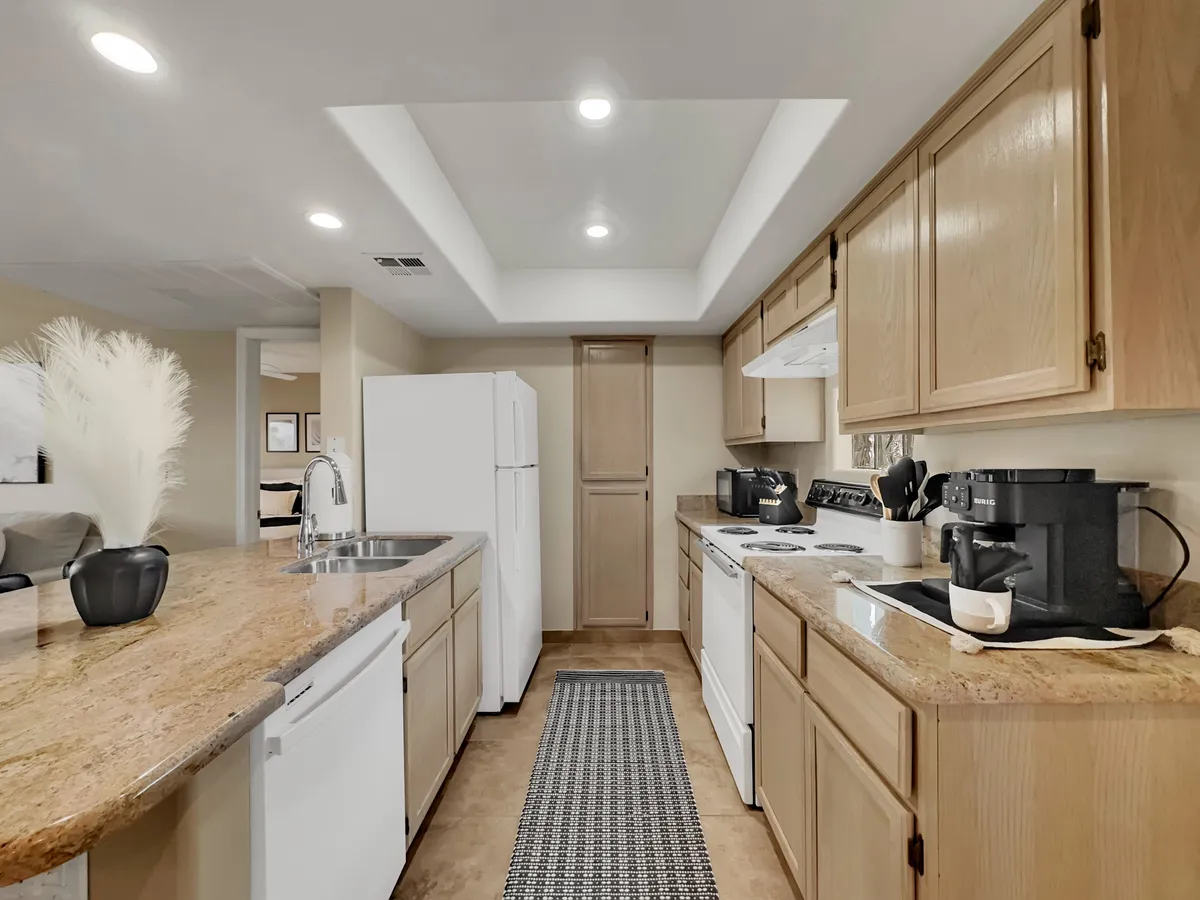 A close-up view of a granite kitchen countertop with white appliances and a black coffee maker. A decorative plant adds a cozy touch, emphasizing practical amenities and stylish finishes.