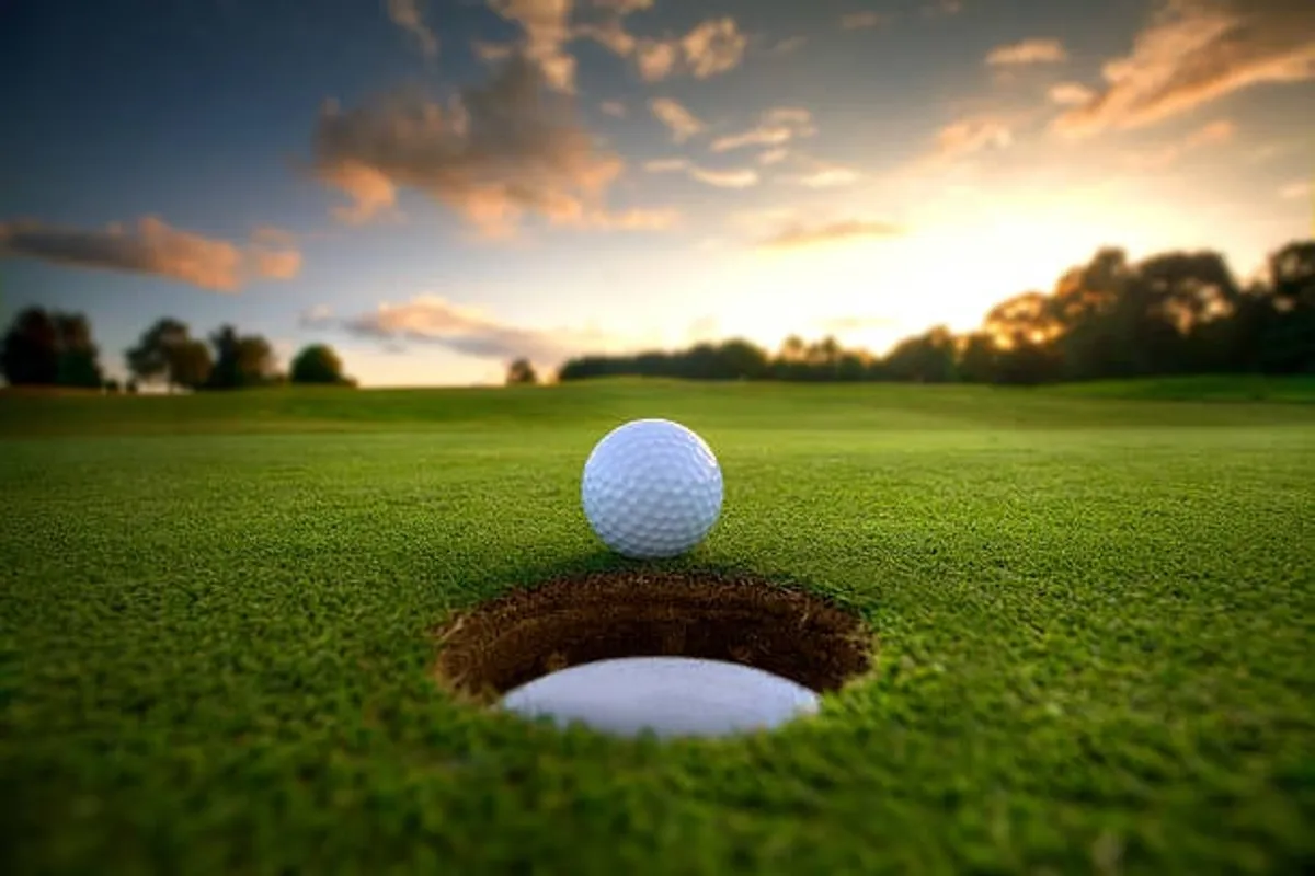 A close-up of a golf ball poised next to a golf hole, set against a backdrop of perfectly manicured green grass. The scene captures the anticipation and satisfaction of a day spent golfing under clear desert skies.