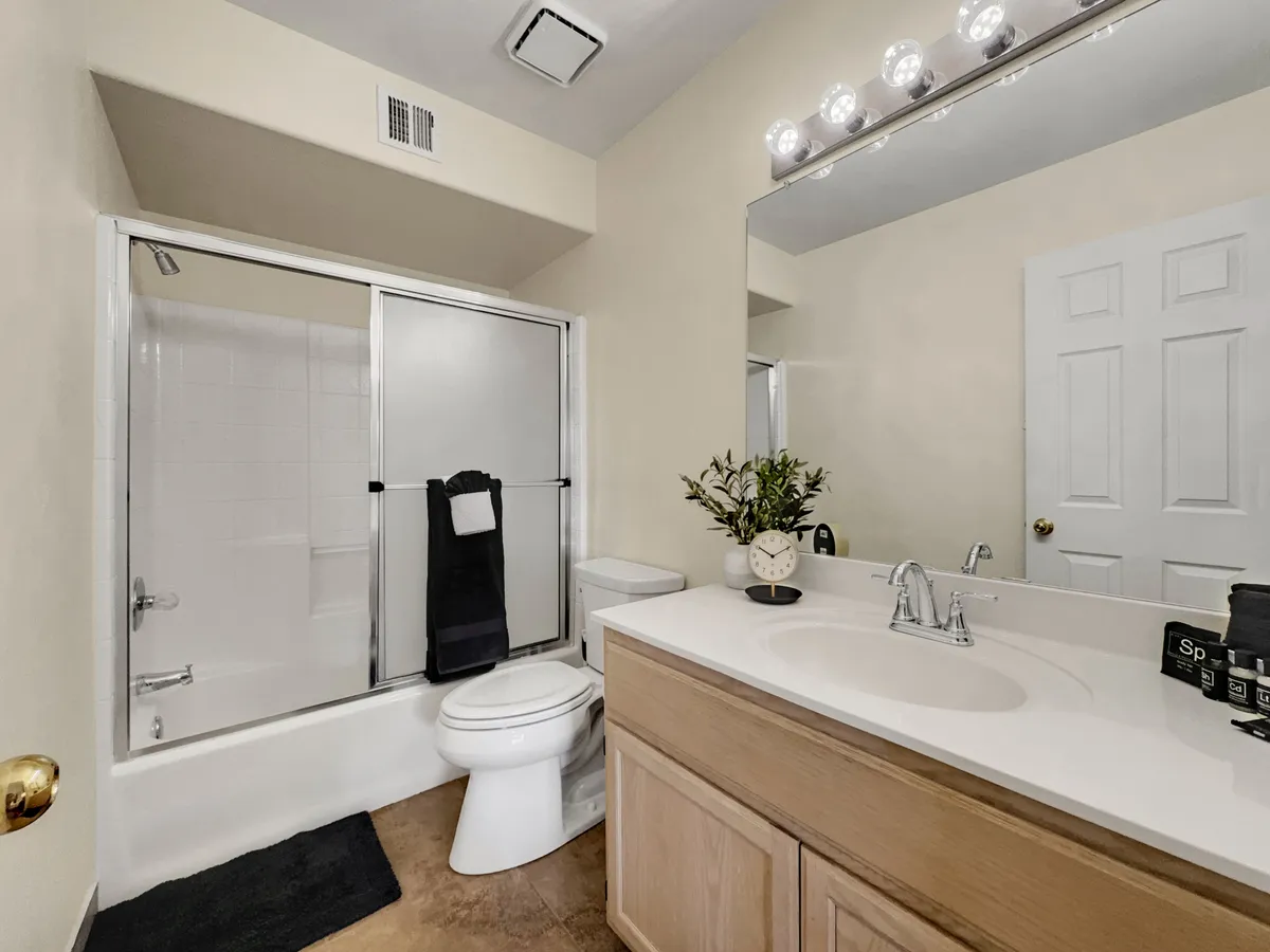 A stylish en-suite bathroom with a sleek vanity counter, large mirror, walk-in shower, and decorative plant. The space feels calm and inviting, designed for soothing baths and refreshing morning routines.