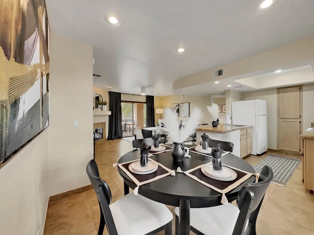 This image highlights a round dining table with black chairs set against a backdrop of a large abstract painting. The open kitchen area, visible with white cabinetry, links the dining and cooking spaces in a warm and welcoming atmosphere.