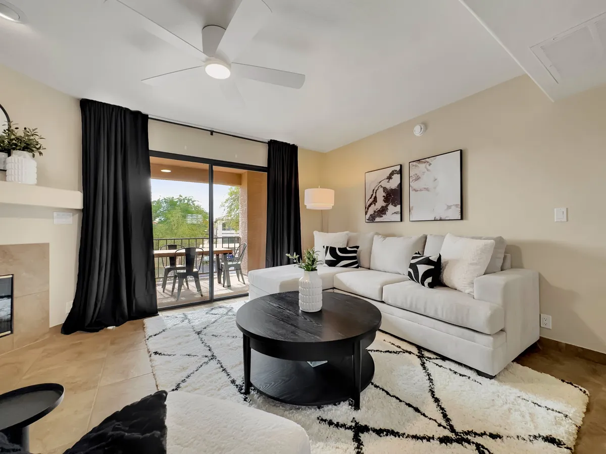 A cozy living room featuring a comfortable sofa, coffee table, soft curtains, wall artwork, and a view of the balcony. The scene is warmly lit and invites relaxation, with easy access to the outdoors and a tranquil atmosphere.