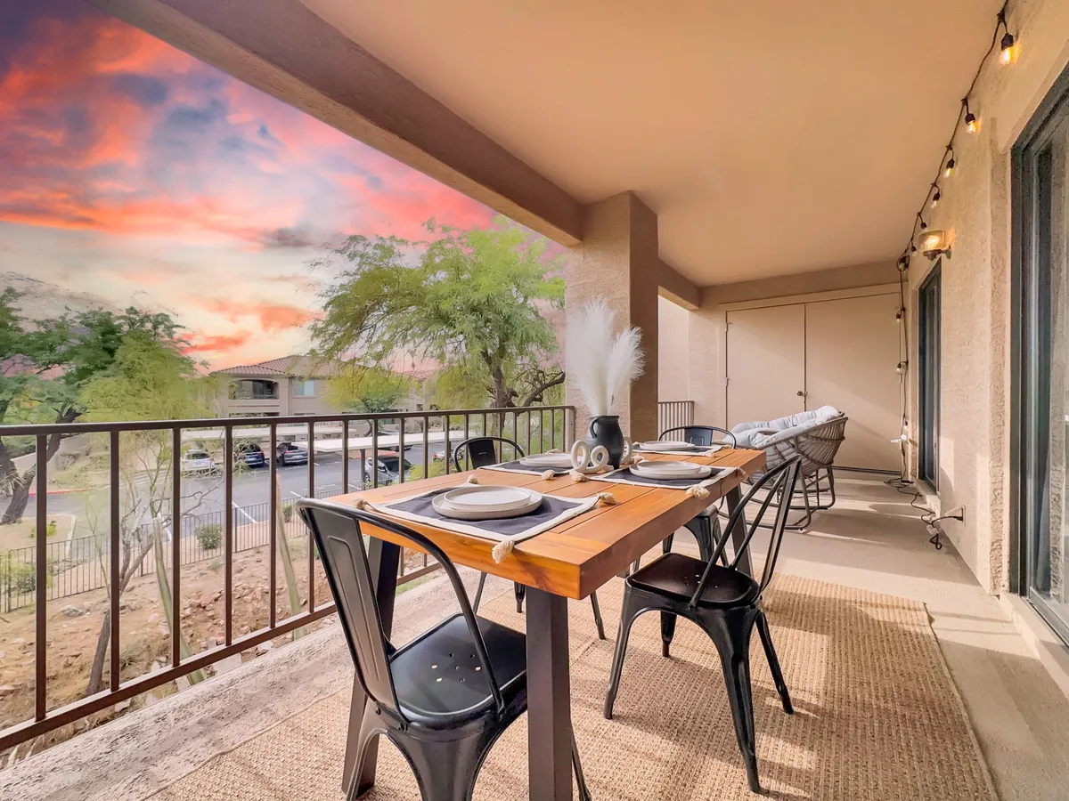An inviting outdoor dining area set for four, with a beautiful sunset sky overhead and decorative touches like a plant arrangement. The warm glow and comfortable arrangement evoke relaxing evenings spent enjoying good food and company after a day on the golf course.